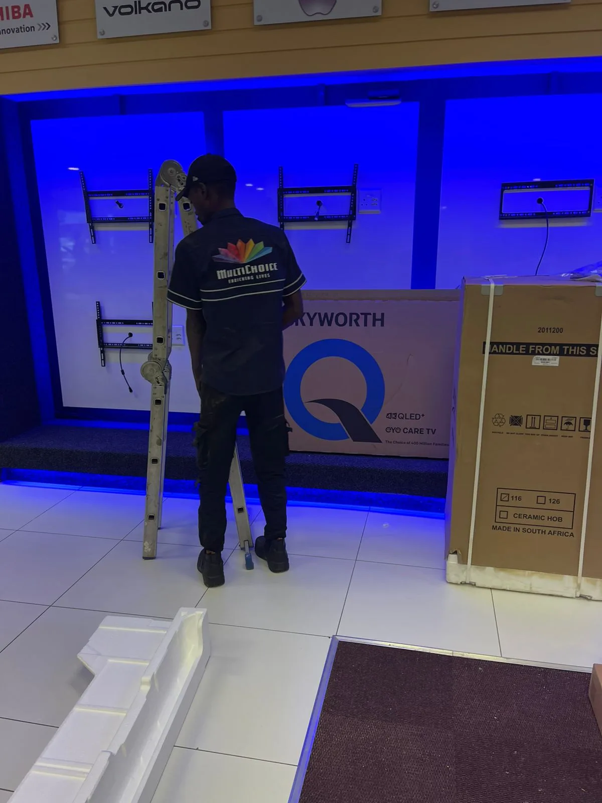 MultiChoice technician reviewing TV wall brackets in a retail showroom